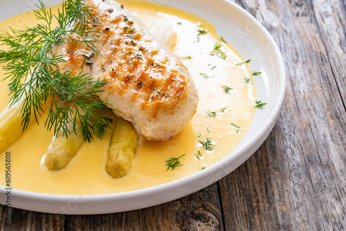 Grilled chicken breast and white asparagus in hollandaise sauce on wooden table
