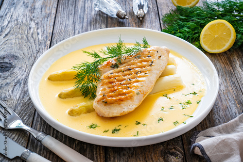 Grilled chicken breast and white asparagus in hollandaise sauce on wooden table
