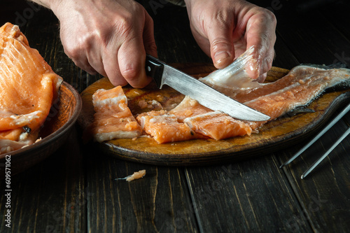 Cutting red fish with a knife on a kitchen cutting board before cooking. Close-up of hands of a cook while cleaning raw fish