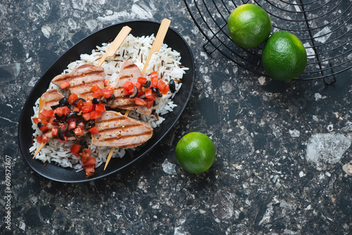 Grilled tuna fillet on skewers with mixed rice, horizontal shot on a dark-brown granite background with space, above view