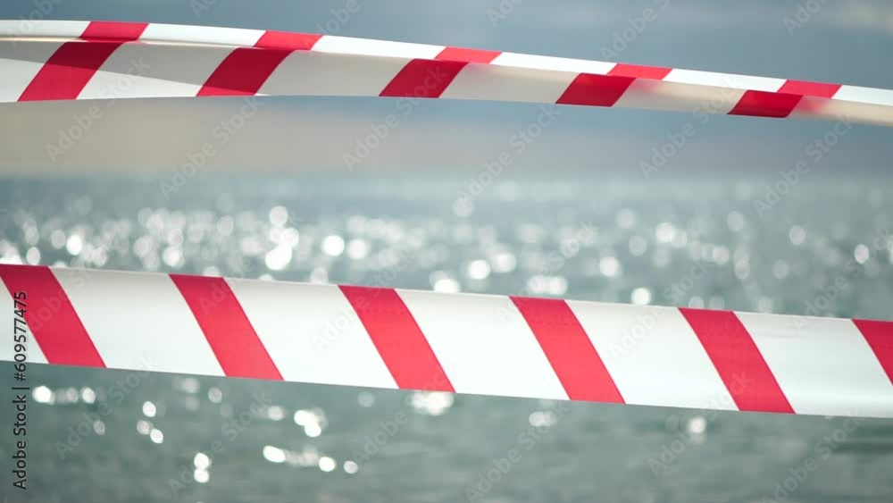 Red white warning tape barrier ribbon swinging in the wind across exotic sea beach background without people. No entry Red White caution tape. No holiday concept, delayed travel, no summer plans Red white warning tape barrier ribbon swinging in the wind across exotic sea beach background without people. No entry Red White caution tape. No holiday concept, delayed travel, no summer plans