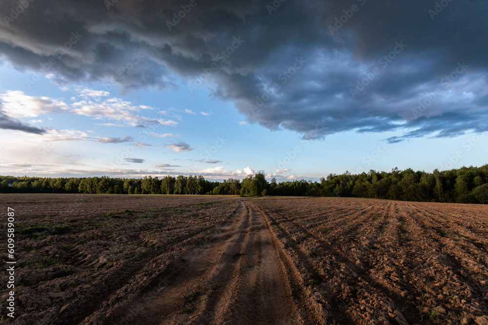 Landscape with plowed agricultural field and dark clouds in the sky
