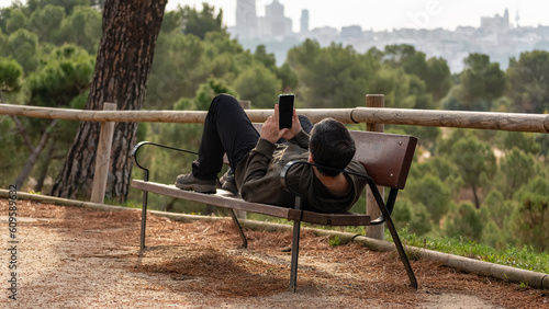 Quadro em tela Man lying on a park bench resting while looking at the mobile phone