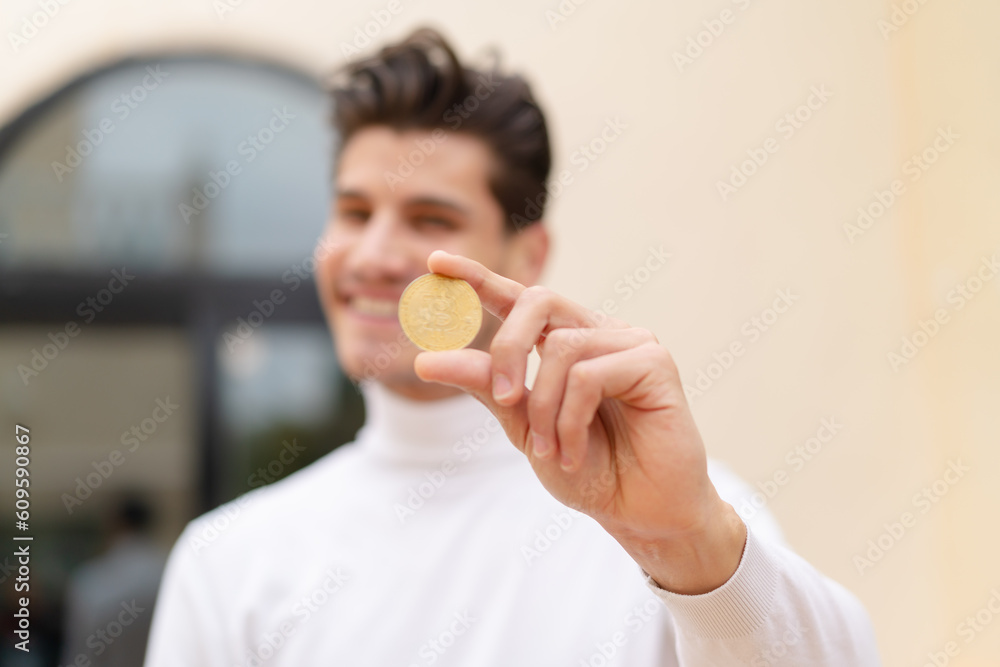 Young caucasian man holding a Bitcoin at outdoors with happy expression Young caucasian man holding a Bitcoin at outdoors with happy expression