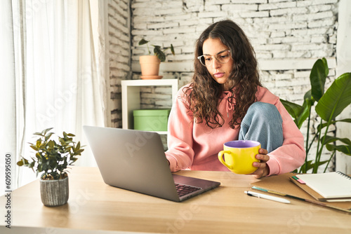 A young woman, focused and productive, working at her home desk with a laptop, sipping coffee, and feeling refreshed.