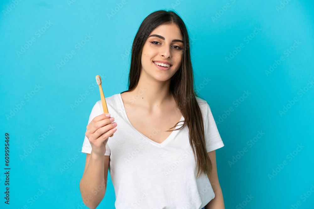 Young caucasian woman brushing teeth isolated on blue background smiling a lot