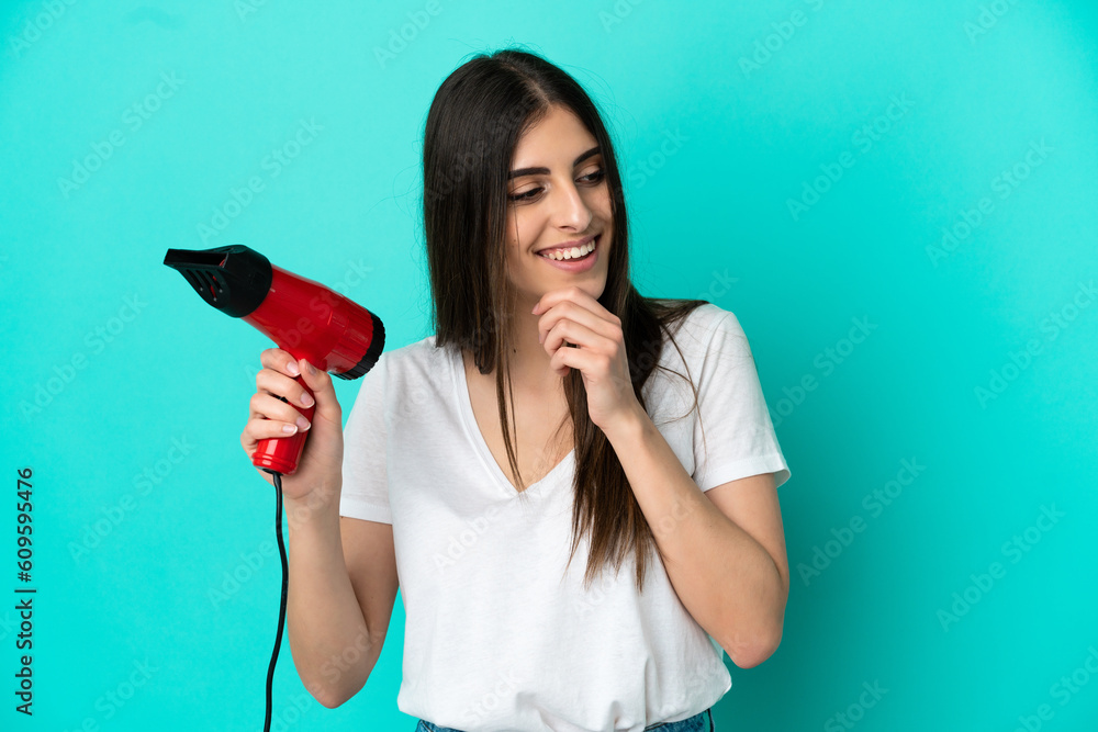 Young caucasian woman holding a hairdryer isolated on blue background thinking an idea and looking side