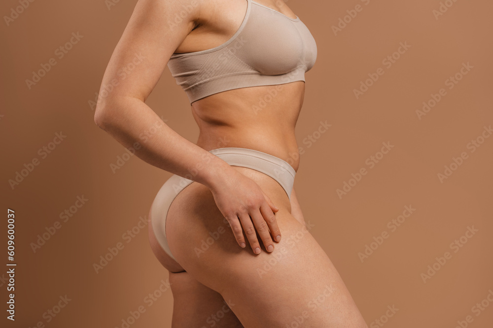 Happy young short hair woman in underwear hugging self against grey background