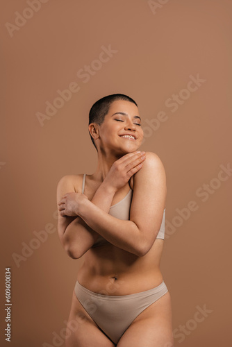 Happy young short hair woman in underwear hugging self against grey background