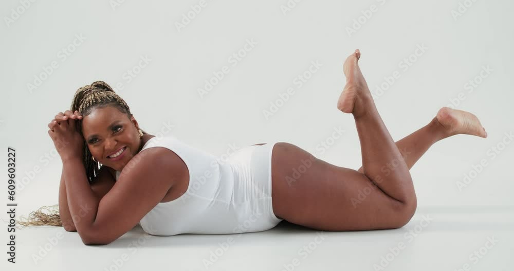 relaxed smiling dreamy plus size lady with raised legs posing in white sexy bodysuit lingerie, on white background Studio alone. attractive black lady is lying on floor, sexy hot fat model has rest relaxed smiling dreamy plus size lady with raised legs posing in white sexy bodysuit lingerie, on white background Studio alone. attractive black lady is lying on floor, sexy hot fat model has rest