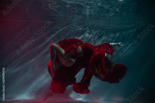a girl under water, in an aquarium, in a pool in a red long dress swims like a mermaid
