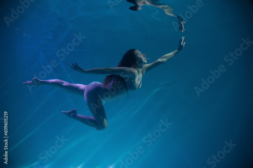 a girl under water, in an aquarium, in a pool in flesh-colored underwear naked swims like a mermaid