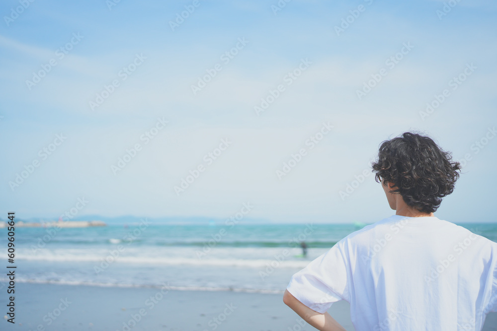 夏の海岸に向かって立つTシャツ姿の男性