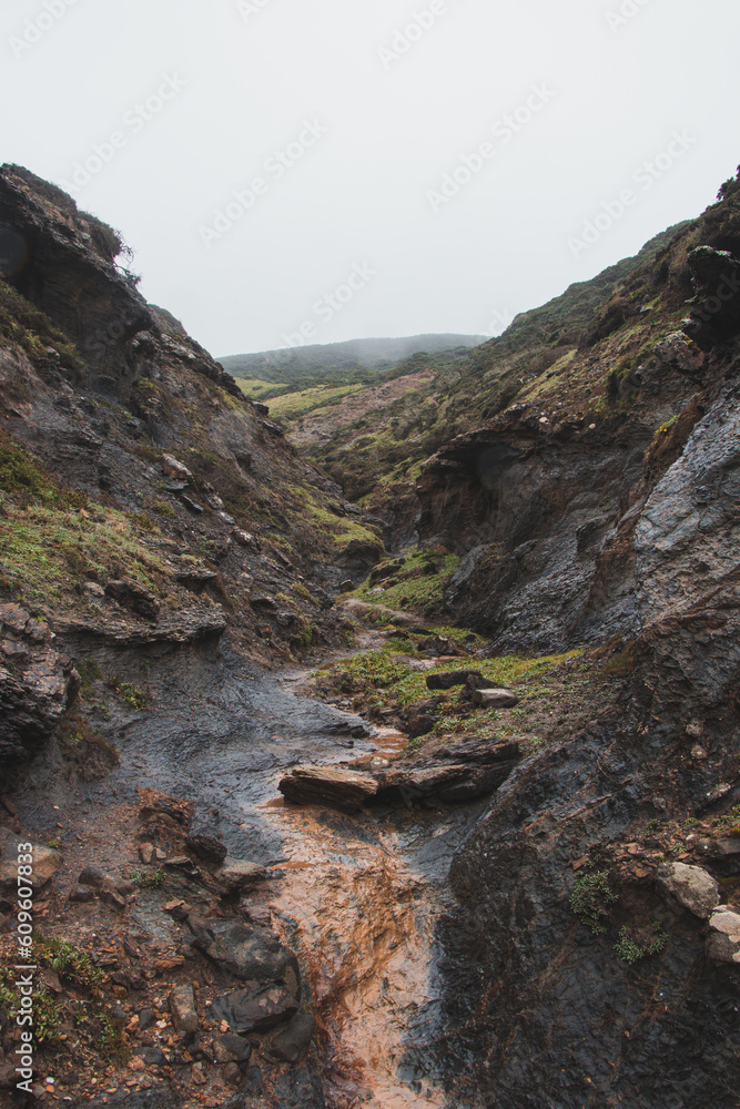Obraz premium Walking through a gorge between two hills in rainy weather in the southwest of Portugal, Algarve region in March. Wandering along the Fisherman Trail