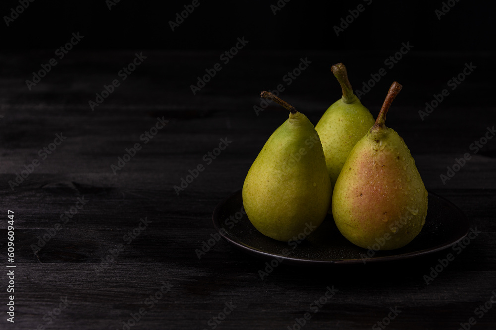 View of green pears with water drops in black plate on dark wooden table, horizontal, with copy space View of green pears with water drops in black plate on dark wooden table, horizontal, with copy space