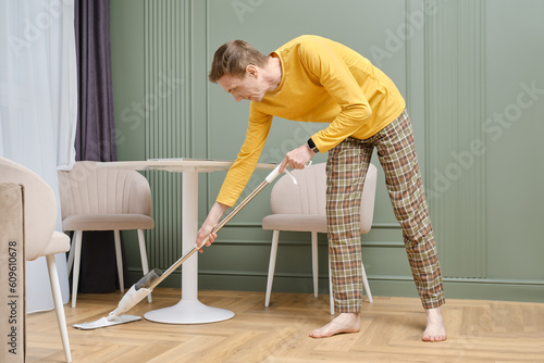 Middle aged man doing housework, mopping floors in living room