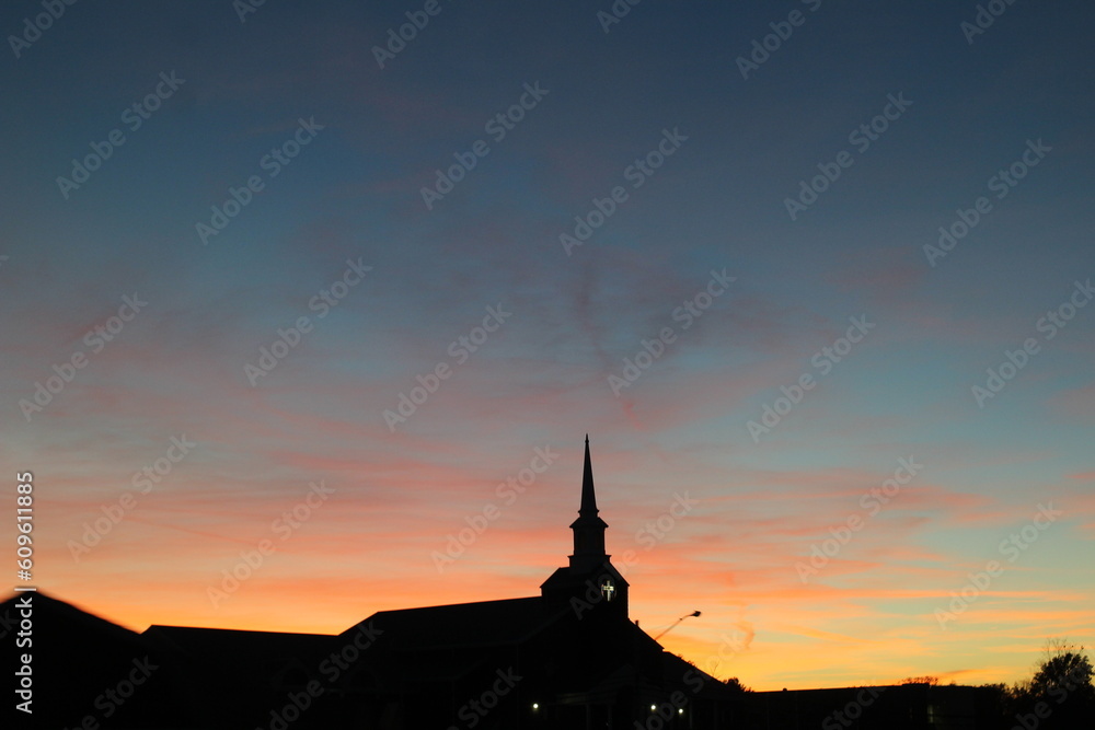 orange and blue sunset with the sillhouette of a church and cross and a bright blue sky and wispy clouds