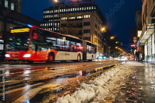 City bus driving through snow covered streets at night. Reflective city lights on the pavement and melting snow. Editorial street photography taken in Luxembourg City, Luxembourg.