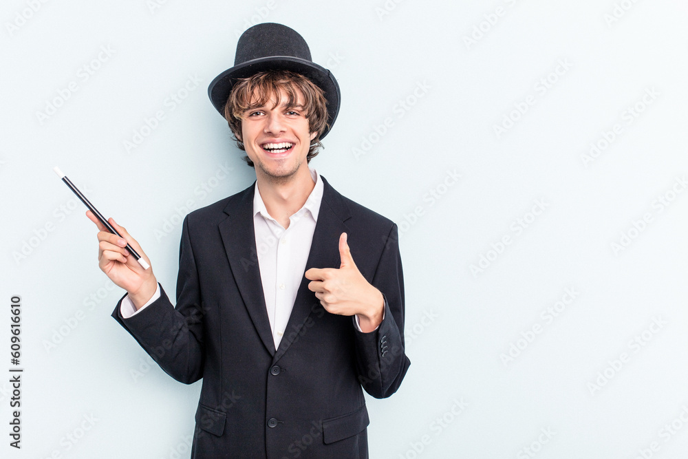 Young magician man holding magic cards isolated on blue background smiling and raising thumb up Young magician man holding magic cards isolated on blue background smiling and raising thumb up