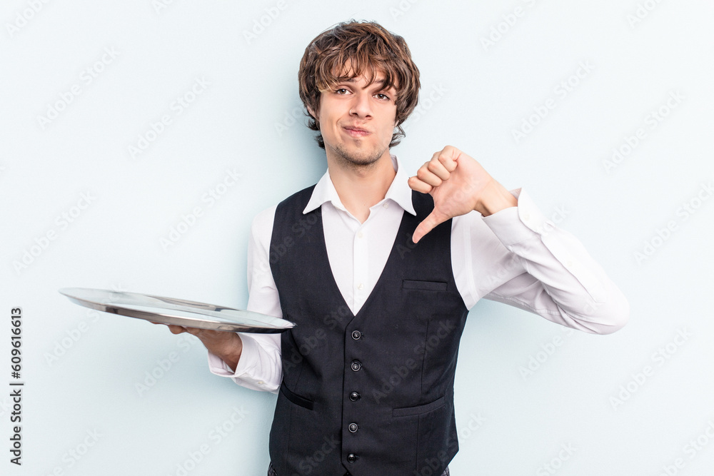 Young caucasian waitress man holding a tray isolated on blue background showing a dislike gesture, thumbs down. Disagreement concept. Young caucasian waitress man holding a tray isolated on blue background showing a dislike gesture, thumbs down. Disagreement concept.