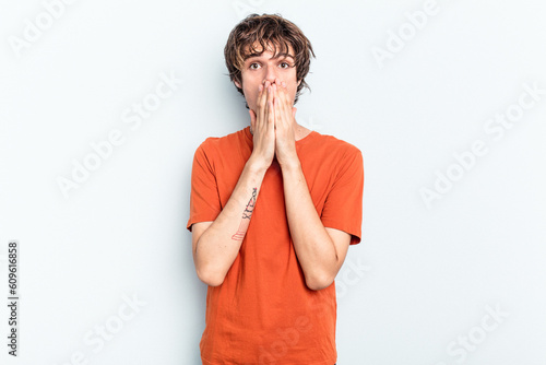 Young caucasian man isolated on blue background shocked covering mouth with hands.