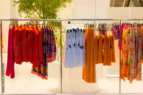 Women's clothing store. Multicolor red, orange blouses hang on hangers in store window. Beauty, fashion business concept. Female clothes shirt, sweater, sundress, dresses. Apparel rack. Shopping sales