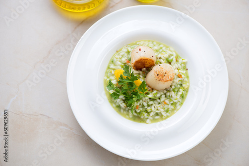 White plate with green pea risotto and seared scallops, elevated view on a beige marble background, horizontal shot