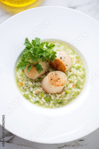 Pea risotto with pan seared sea scallops served in a white plate, vertical shot, closeup, selective focus