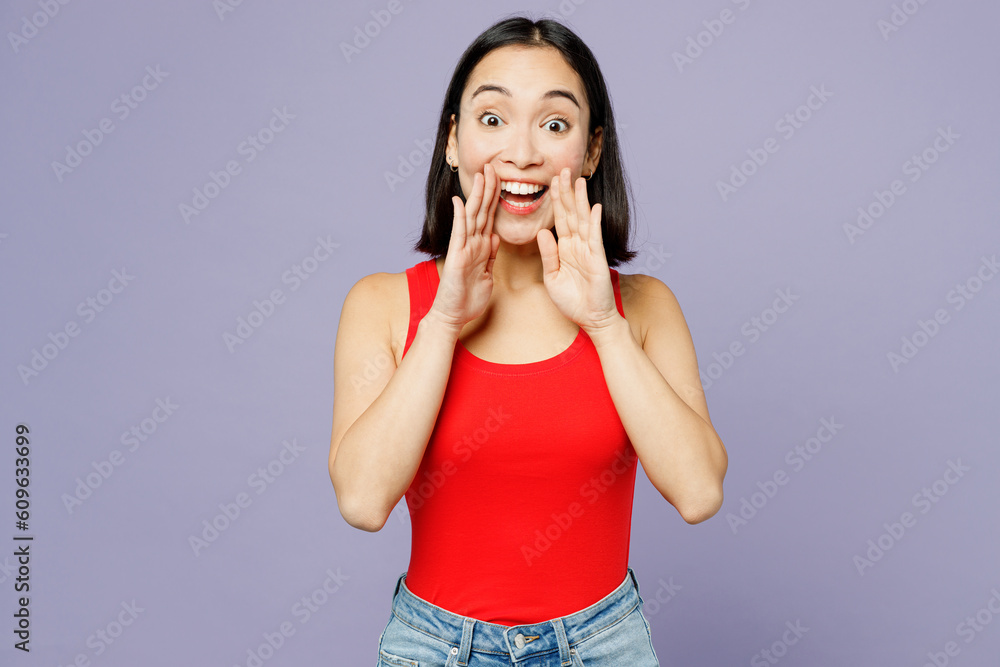 Young woman of Asian ethnicity wear casual clothes red tank shirt scream sharing hot news about sales discount with hands near mouth isolated on plain pastel light purple background studio portrait. Young woman of Asian ethnicity wear casual clothes red tank shirt scream sharing hot news about sales discount with hands near mouth isolated on plain pastel light purple background studio portrait.