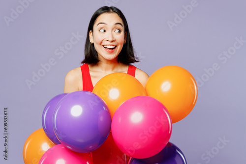 Young excited woman of Asian ethnicity she wear casual clothes red tank shirt hold bunch of colorful air balloons look aside isolated on plain pastel light purple background studio. Lifestyle concept.