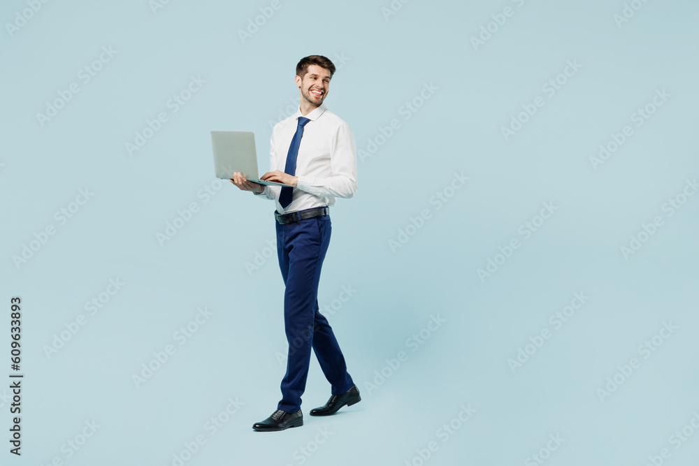Full body side view young employee IT business man corporate lawyer wearing classic formal shirt tie work in office hold use work on laptop pc computer isolated on plain pastel blue background studio. Full body side view young employee IT business man corporate lawyer wearing classic formal shirt tie work in office hold use work on laptop pc computer isolated on plain pastel blue background studio.