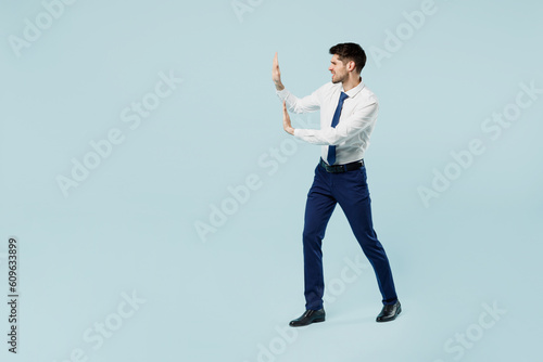 Full body young employee IT business man corporate lawyer in classic formal shirt tie work in office pov push invisible object with copy space isolated on plain light blue background studio portrait