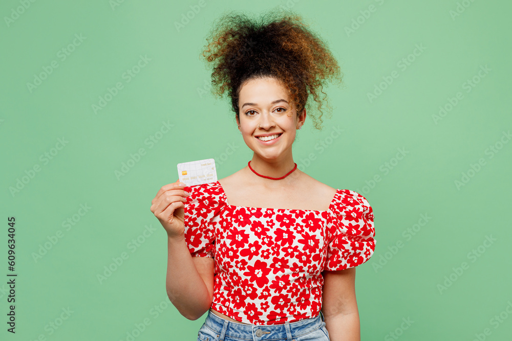 Young smiling fun happy woman she wearing casual clothes red blouse hold in hand mock up of credit bank card isolated on plain pastel light green color background studio portrait. Lifestyle concept. Young smiling fun happy woman she wearing casual clothes red blouse hold in hand mock up of credit bank card isolated on plain pastel light green color background studio portrait. Lifestyle concept.