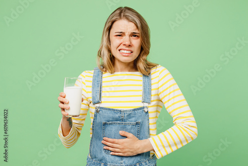 Sick unhealthy ill allergic sad woman has red watery eyes runny stuffy sore nose suffer from allergy trigger symptoms hay fever hold glass of milk hold belly isolated on plain green background studio Fototapet