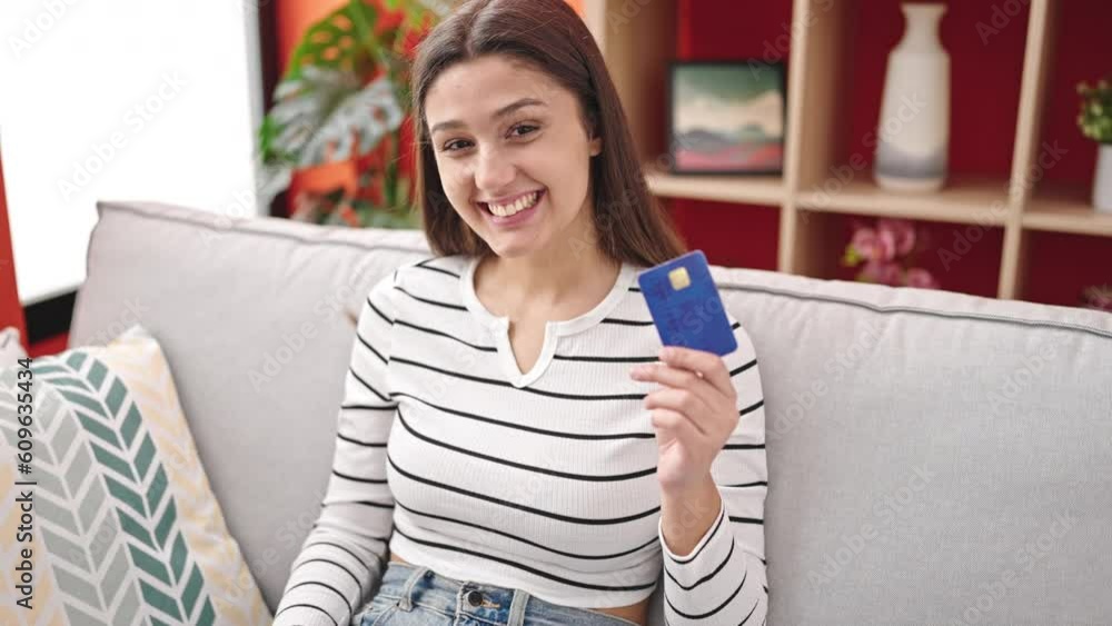 Young beautiful hispanic woman shopping with laptop and credit card sitting on sofa at home Young beautiful hispanic woman shopping with laptop and credit card sitting on sofa at home