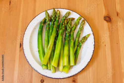 Green boiled asparagus in a plate on a wooden table