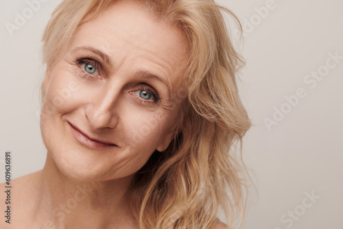 Beautiful blond middle aged woman smiling face looking at camera portrait. Elegant mature lady no makeup 50 years old close-up isolated on white studio. Women's health, cosmetology, skin care concept