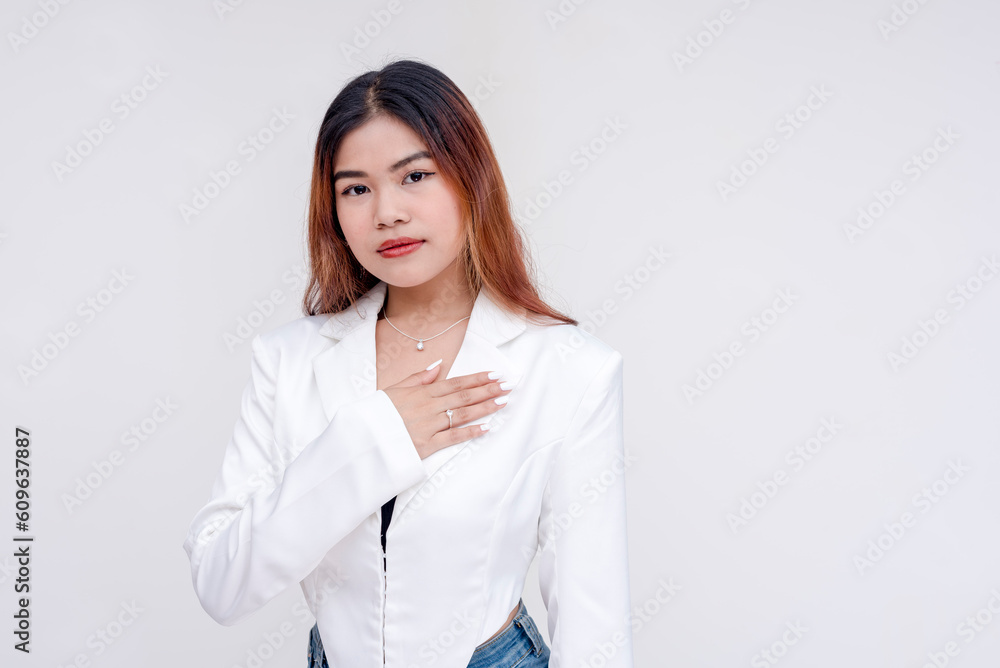 A serious and earnest young woman looking at the camera while holding one hand to her chest. Isolated on a white background. A serious and earnest young woman looking at the camera while holding one hand to her chest. Isolated on a white background.