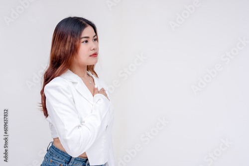 A serious young woman facing to the right while holding one hand to her chest. Isolated on a white background.