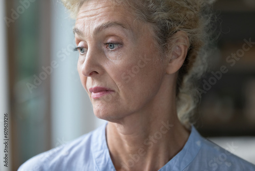 Bored sad lonely pretty senior woman looking at window away, thinking over problem, trouble, suffering from mental disorder, Alzheimer disease. Upset mature lady close up portrait
