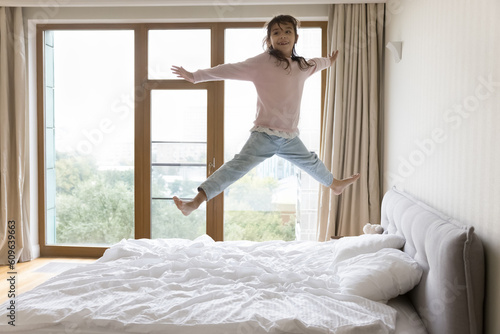 Happy carefree little child jumping on bed mattress at home, flying in air with open arms and legs, laughing, smiling, playing active games, enjoying activities, leisure, motion, having fun alone