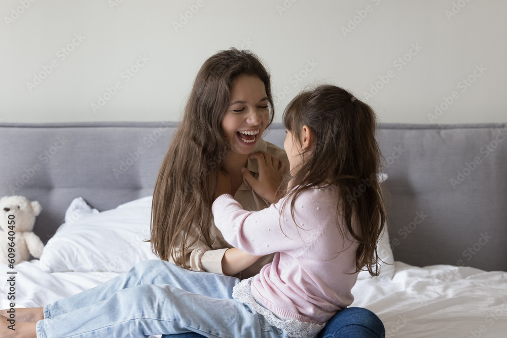 Joyful young mother tickling little preschool kid girl, playing active games with daughter on bed, having fun, laughing, smiling, enjoying family weekend, leisure time, motherhood Joyful young mother tickling little preschool kid girl, playing active games with daughter on bed, having fun, laughing, smiling, enjoying family weekend, leisure time, motherhood