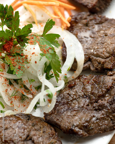 Pieces of fried beef with onions and carrots on white plate. Fried meat with vegetables. Serving dish. Close-up. View from above. Soft focus. photo