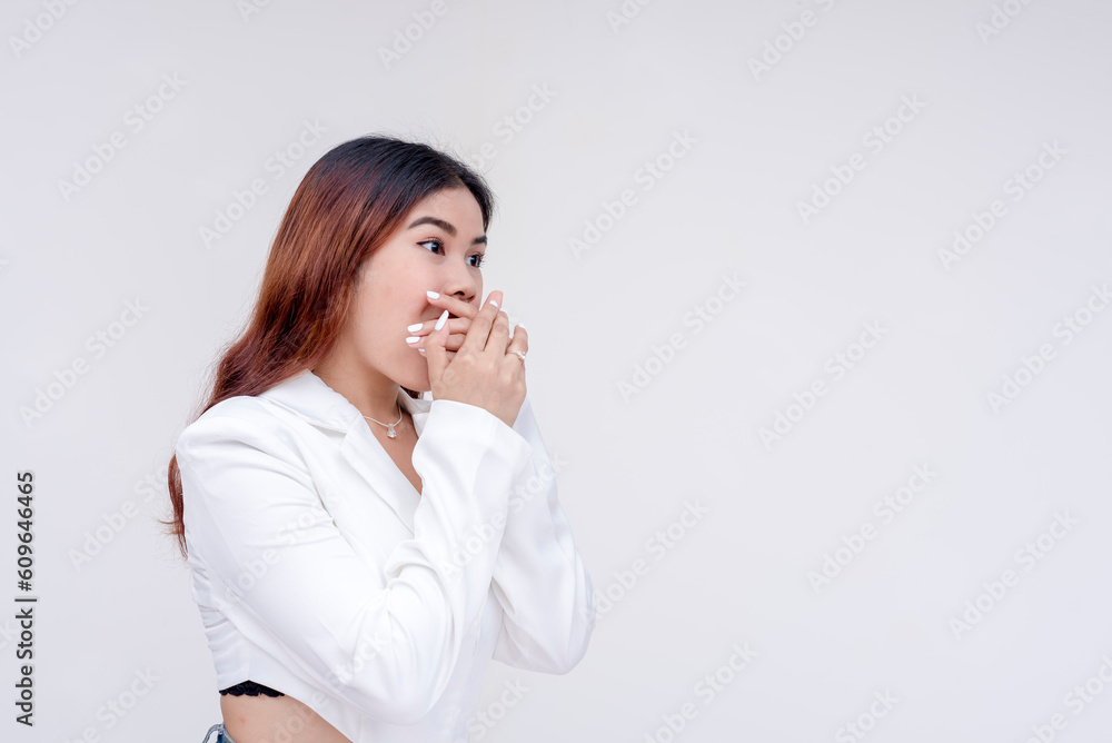 A surprised young woman with eyebrows raised covering her mouth with both hands in shock and facing right. Isolated on a white background. A surprised young woman with eyebrows raised covering her mouth with both hands in shock and facing right. Isolated on a white background.