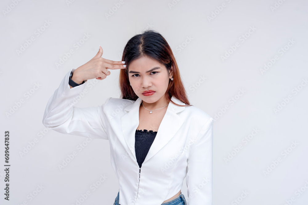 An angry young woman pointing a finger gun to her head while pointedly looking at the camera. Isolated on a white background. An angry young woman pointing a finger gun to her head while pointedly looking at the camera. Isolated on a white background.