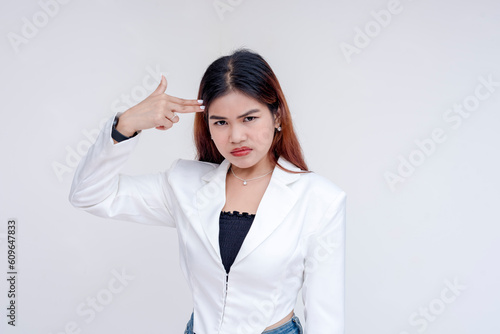 An angry young woman pointing a finger gun to her head while pointedly looking at the camera. Isolated on a white background. photo