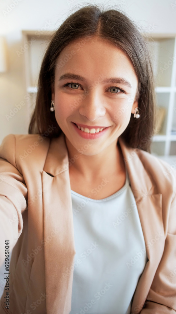 Happy selfie. Warm smile. Sincere emotions. Positive cheerful attractive  beautiful young business woman taking photo in light interior. Stock Photo