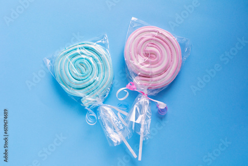 Candy on a stick. Spiral sweets. Candies of two colors pink and blue on a blue background. Candies in plastic packaging.