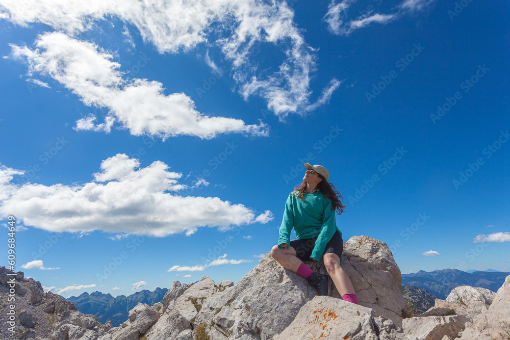 Girl sitting on a boulder looking at the sky during a hike in the Dolomites, Mount Latemar, Trentino, Italy. Traveling photography and outdoor sport activity concept