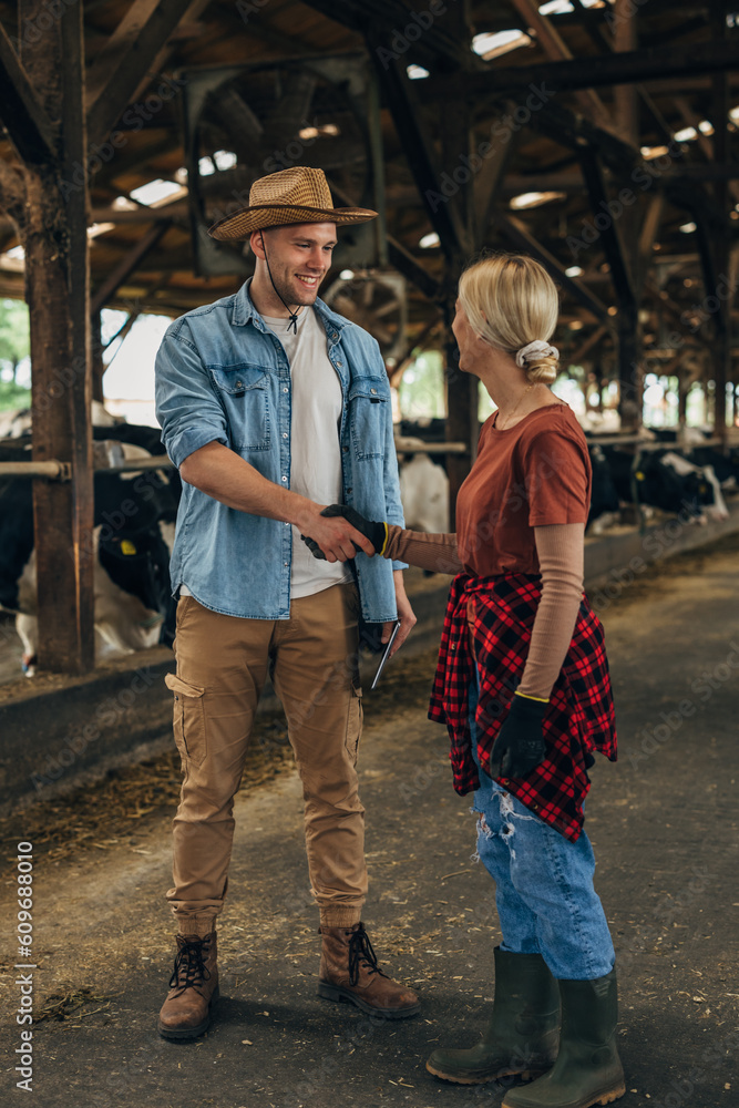 A man with a leghorn shakes hands with a woman working in a stable. A man with a leghorn shakes hands with a woman working in a stable.